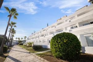 a large white building with palm trees and a sidewalk at Flipflop Cala Mandia in Cala Romàntica