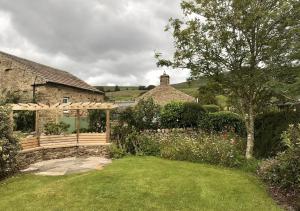 a garden with a wooden pergola in front of a house at Seata Barn in Askrigg