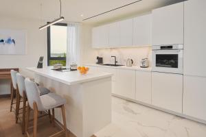 una cocina blanca con armarios blancos y taburetes de bar en Petram Resort & Residences en Savudrija