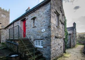 阿斯科里格的住宿－Rooks Cottage，一座古老的石头房子,设有红色的门和楼梯