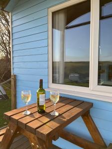 a bottle of wine and two glasses on a picnic table at Coral Shepherds Hut in Penally