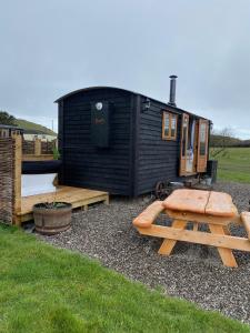 una pequeña casa negra con un banco y una mesa en Silver Fern Glamping, en Aberystwyth