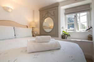 a white bedroom with a large white bed with a mirror at Cottage on the Dart- Riverside Fishermans Cottage in Stoke Gabriel