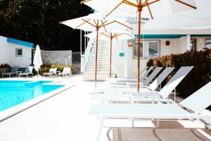 una fila de sillas y sombrillas blancas junto a una piscina en Principe Alogna Hotel & SPA en Altavilla Milicia