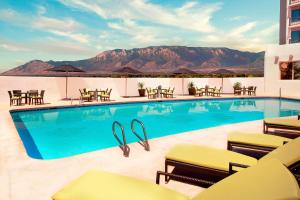 uma piscina com cadeiras e mesas e montanhas ao fundo em Sheraton Albuquerque Airport Hotel em Albuquerque