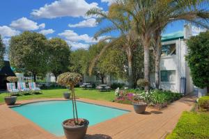 a swimming pool with palm trees and a house at Protea Hotel by Marriott Polokwane Landmark in Polokwane