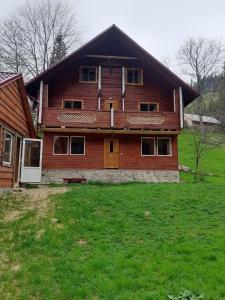a large wooden house with a green field in front of it at Крайня Хата in Synevyrsʼka Polyana