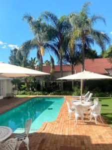 - une piscine avec des chaises, une table et des parasols dans l'établissement Brooklyn Place, à Pretoria