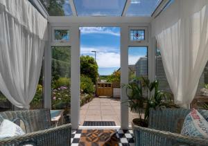 a conservatory with white curtains and chairs on a patio at Mary-Rose Cottage in Saint Erth