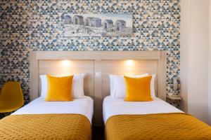 two beds in a hotel room with yellow pillows at Hôtel de Lion sur Mer in Lion-sur-Mer