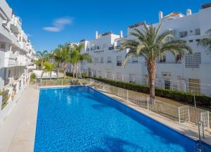 a swimming pool with palm trees and buildings at 2051-New 3 bedrooms on golf in Estepona