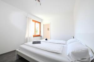 2 witte bedden in een witte kamer met een raam bij Comfortably Losone in Losone