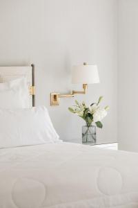 a white bed with a lamp and a vase of flowers at The Oaks Waterfront in Saint Michaels