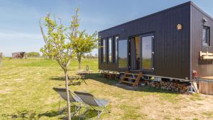 ein schwarzes winziges Haus mit zwei Stühlen und einem Baum in der Unterkunft Tiny House haras Normand - 20 minutes d'Étretat 