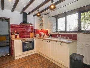 a kitchen with white cabinets and red brick walls at The Coach House in Holywell