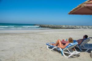 a man and woman sitting in lawn chairs on the beach at Beachfront Holiday Homes in Ajman 