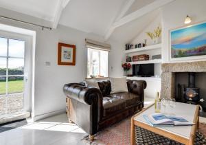 a living room with a leather couch and a fireplace at The Byre - Sennen in Sennen