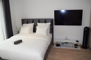 um quarto com uma cama com lençóis brancos e uma televisão de ecrã plano em LAWSON'S GOLD BELL STUDIO em Luxemburgo