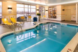 a swimming pool in a hotel lobby with yellow chairs at Fairfield Inn & Suites by Marriott Utica in Utica