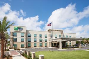 Holiday Inn Express & Suites Gulf Breeze - Pensacola Area, an IHG Hotel في غولف بريز: مبنى مكتب مع علم أمريكي أمامه