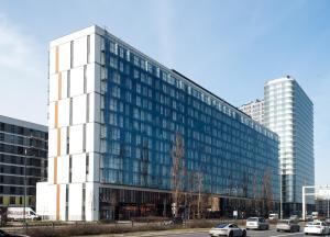 un edificio de cristal alto con coches estacionados frente a él en Prymasa Tysiąclecia 83A -E- dwa pokoje i garaż Perfect Apart en Varsovia