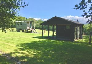 a small shed in a grassy field with a house at Foxgloves and Fairytales Hut with Hot Tub in Llanwrda