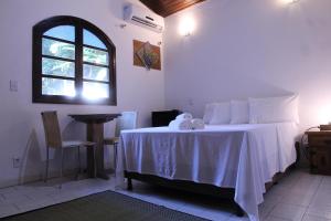 a bedroom with a bed with a table and a window at Hospedaria Bem Te Vi Arraial d'Ajuda in Arraial d'Ajuda