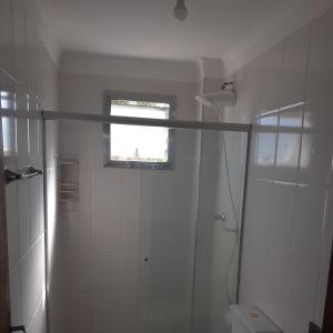 a white bathroom with a shower and a window at Apt 204 Frente Para o Mar e Piscina Village das Ondas in Piúma