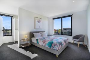 a bedroom with a bed and a chair and windows at Bliss at South Beach in Port Fairy