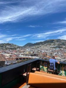 un hombre sentado en un balcón con vistas a una ciudad en Hostal La Guayunga RoofTop en Quito