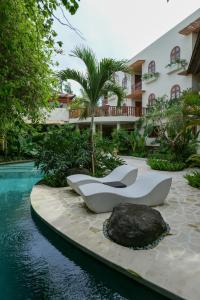 a swimming pool with two white chairs next to a building at Kresna By The Sea By Kresna Hospitality in Seminyak