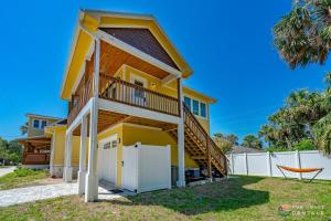 a yellow house with a deck and a fence at Lovely Guesthouse Loft with Balcony and Hammock STEPS from the Beach! in New Smyrna Beach