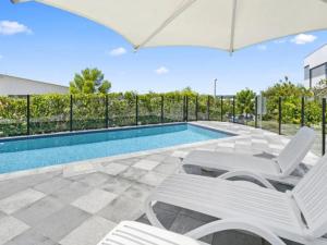 uma piscina com duas cadeiras brancas e um guarda-sol em Luxury Private Queen Room with Balcony & Bathroom in Shared Apartment Panorama Gold Coast em Gold Coast