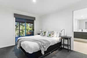 a white bedroom with a large bed and a window at Fuller Holidays - Leah's Retreat - Relax in nature in Bangalow