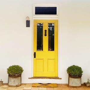 een gele deur op een wit huis met twee potplanten bij Coastal luxury: five minute stroll to the beach. in Queenscliff