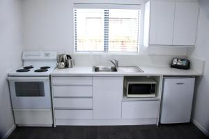 a white kitchen with a sink and a stove at Camelot On Ulster in Hamilton