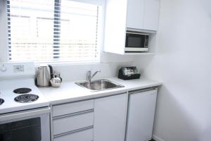 a white kitchen with a sink and a microwave at Camelot On Ulster in Hamilton