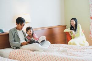 a man and a woman sitting on a bed with a child at Hotel Nikko Huis Ten Bosch in Sasebo