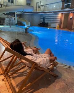 una mujer sentada en una silla junto a una piscina en Platium Spa&Resort, en Kozin