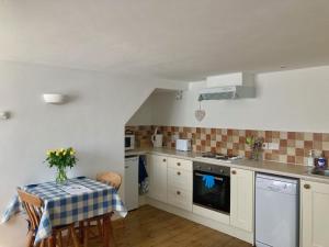 uma cozinha com armários brancos e uma mesa com uma toalha de mesa em Cloister Park Cottages em Frithelstock