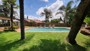 a swimming pool in a yard with palm trees at Klein Bosveld Guest House in eMalahleni