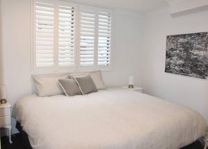 a white bedroom with a bed with pillows and a window at Lavish 3-bedroom ocean apartment in Wollongong in Wollongong