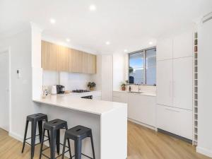 a white kitchen with white cabinets and black stools at Lavish 3-bedroom ocean apartment in Wollongong in Wollongong