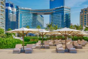 NH Collection Dubai The Palm في دبي: شاطئ فيه كراسي ومظلات امام المباني