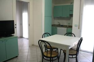 TV y cocina con mesa y sillas blancas. en Residence Le Vele en Cattolica