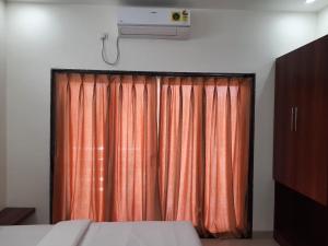 1 dormitorio con cortina naranja y TV en Raapan Beach Resort en Malvan