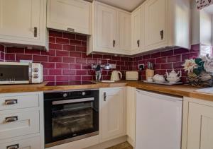 a kitchen with white cabinets and a red brick wall at Hillyard in Hawes