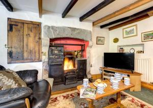 Foss Garth Cottage في Thwaite: غرفة معيشة فيها موقد وتلفزيون