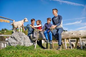 um homem e três crianças sentados numa cerca com ovelhas em Reka-Feriendorf Urnäsch em Urnäsch