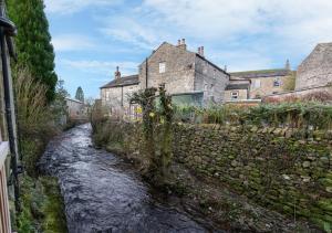 a river in a town with houses and a stone wall at Fellside in Kettlewell